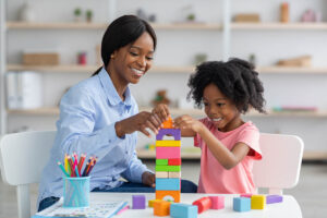 Woman plays blocks with daughter as she considers the cost of play therapy